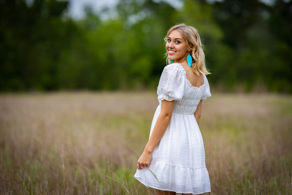 Smiling girl in white dress standing in field.