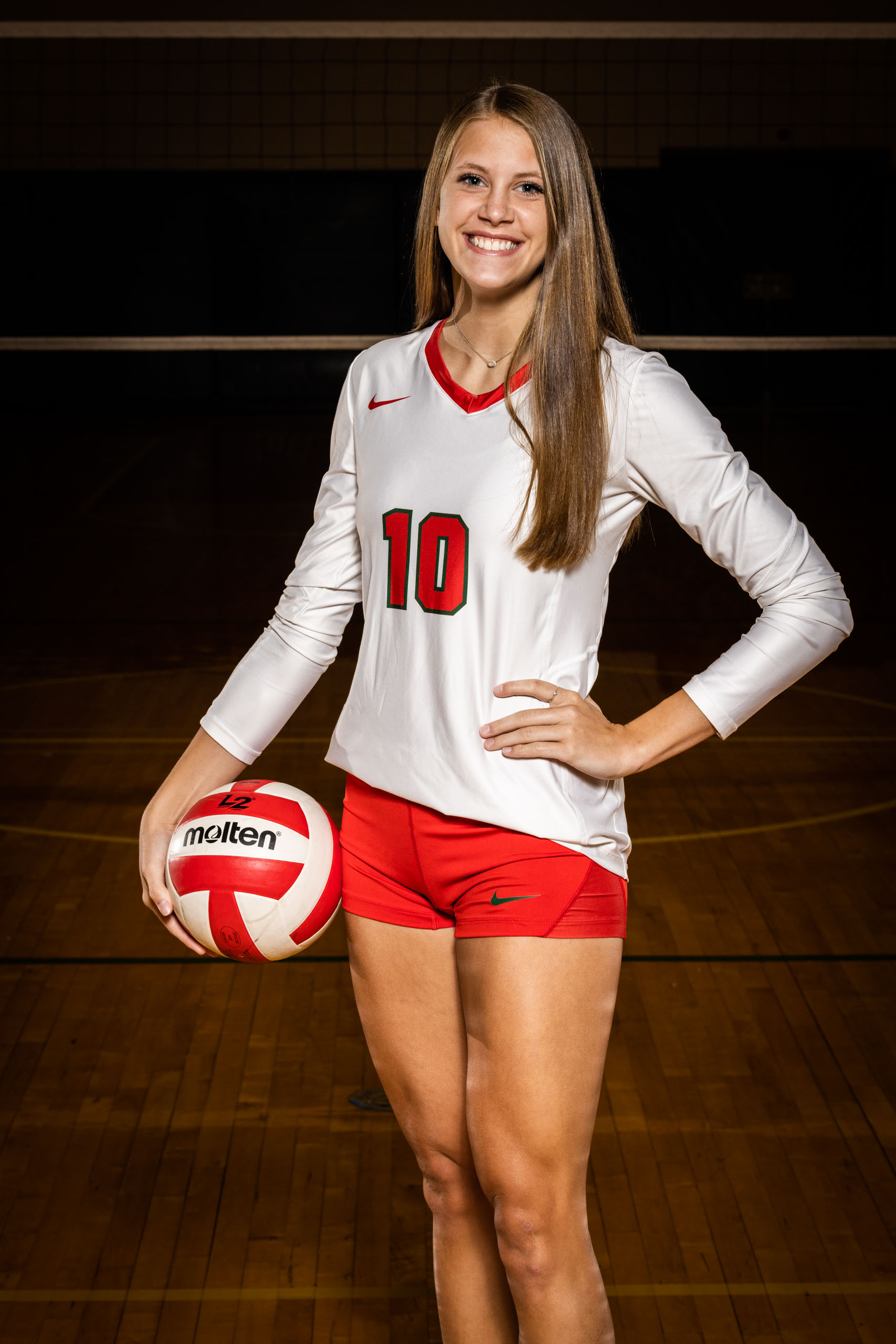 Female volleyball player posing in gym with dramatic lighting.