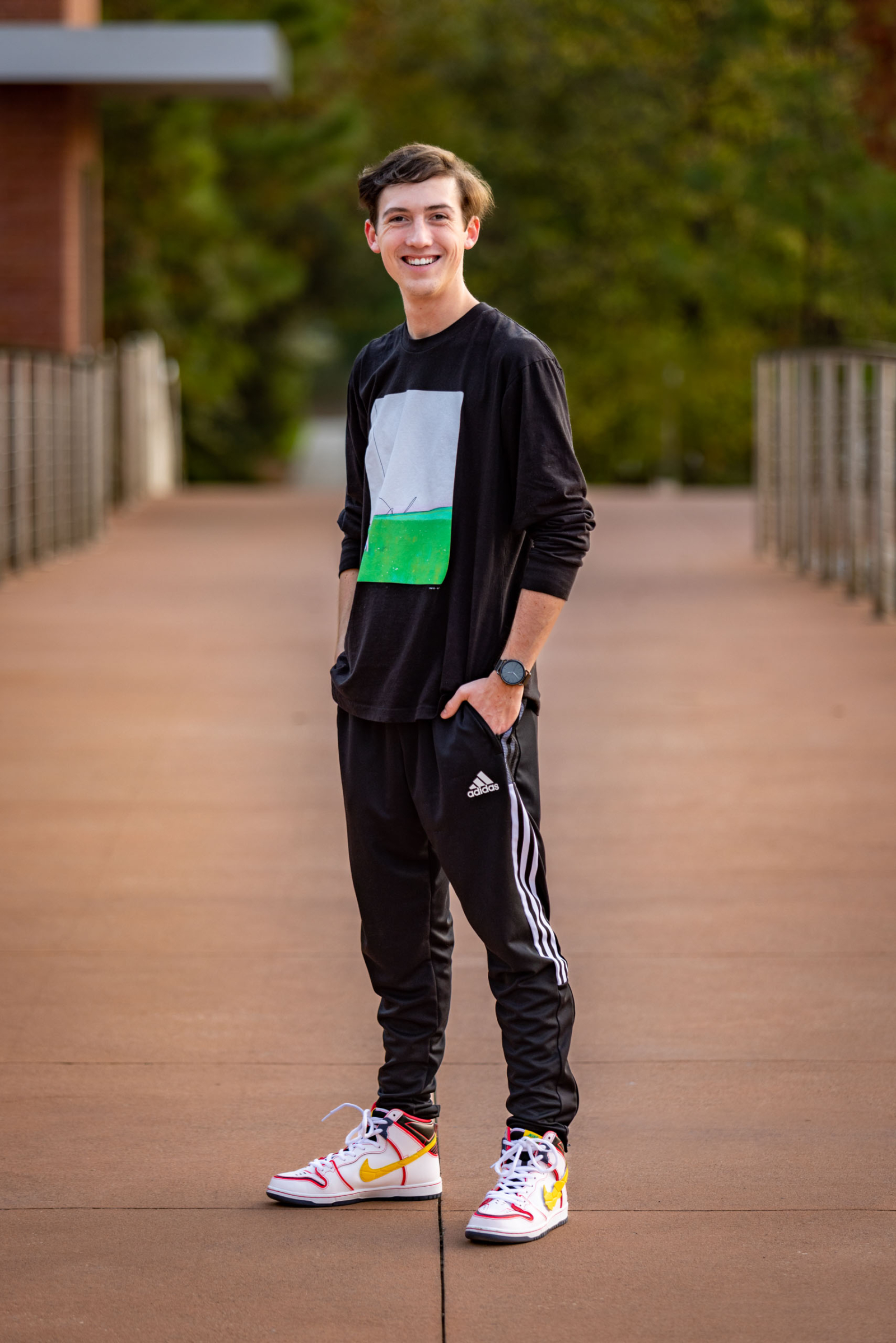 High school senior boy with high top Nike sneakers standing on bridge.