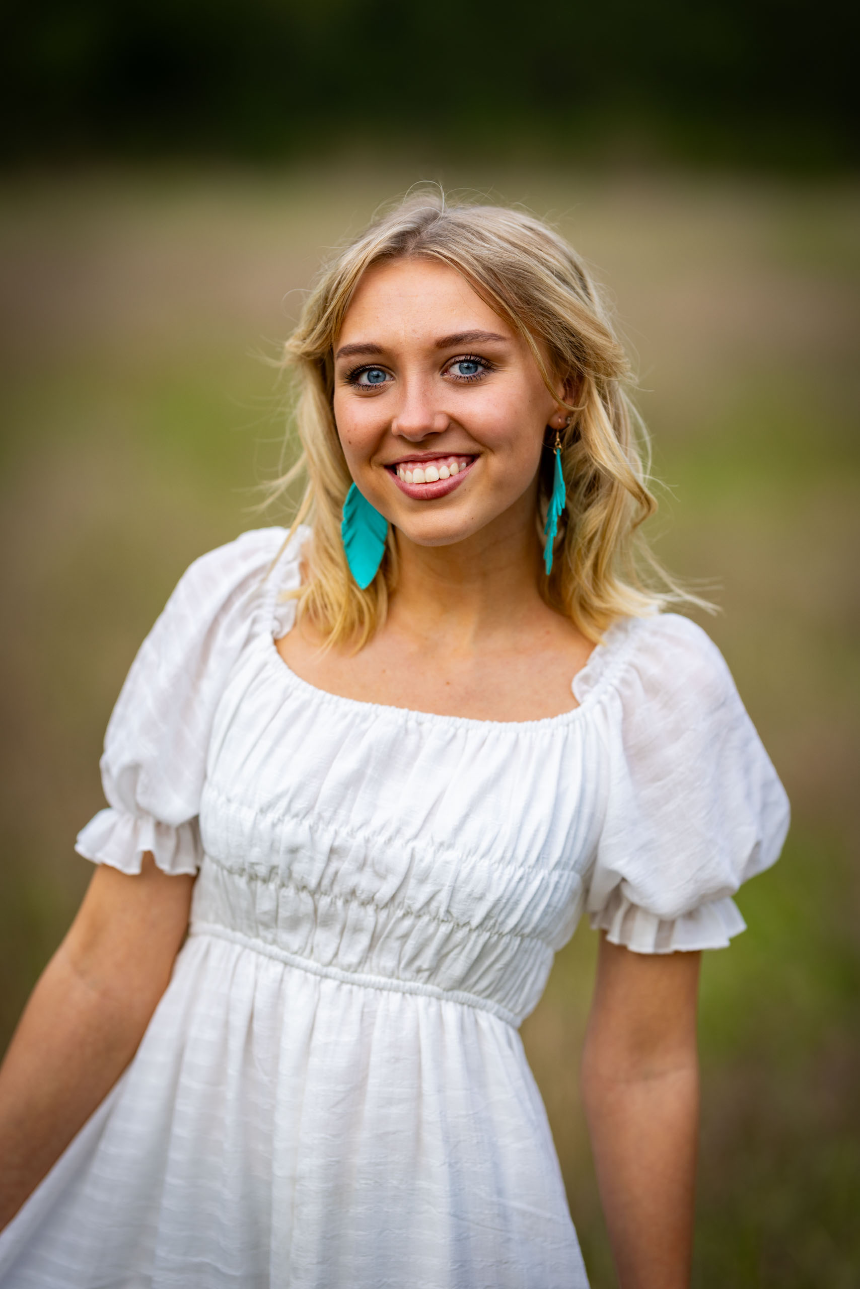 Smiling girl in white dress standing in field.
