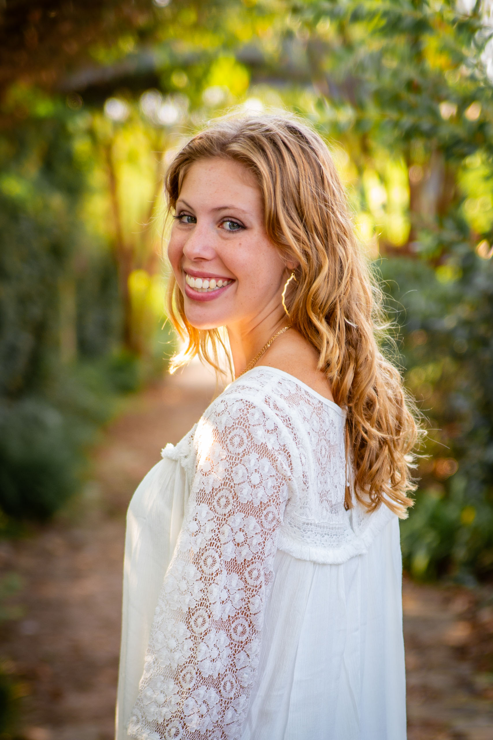 Girl in white dress on pathway, backlit by sun.